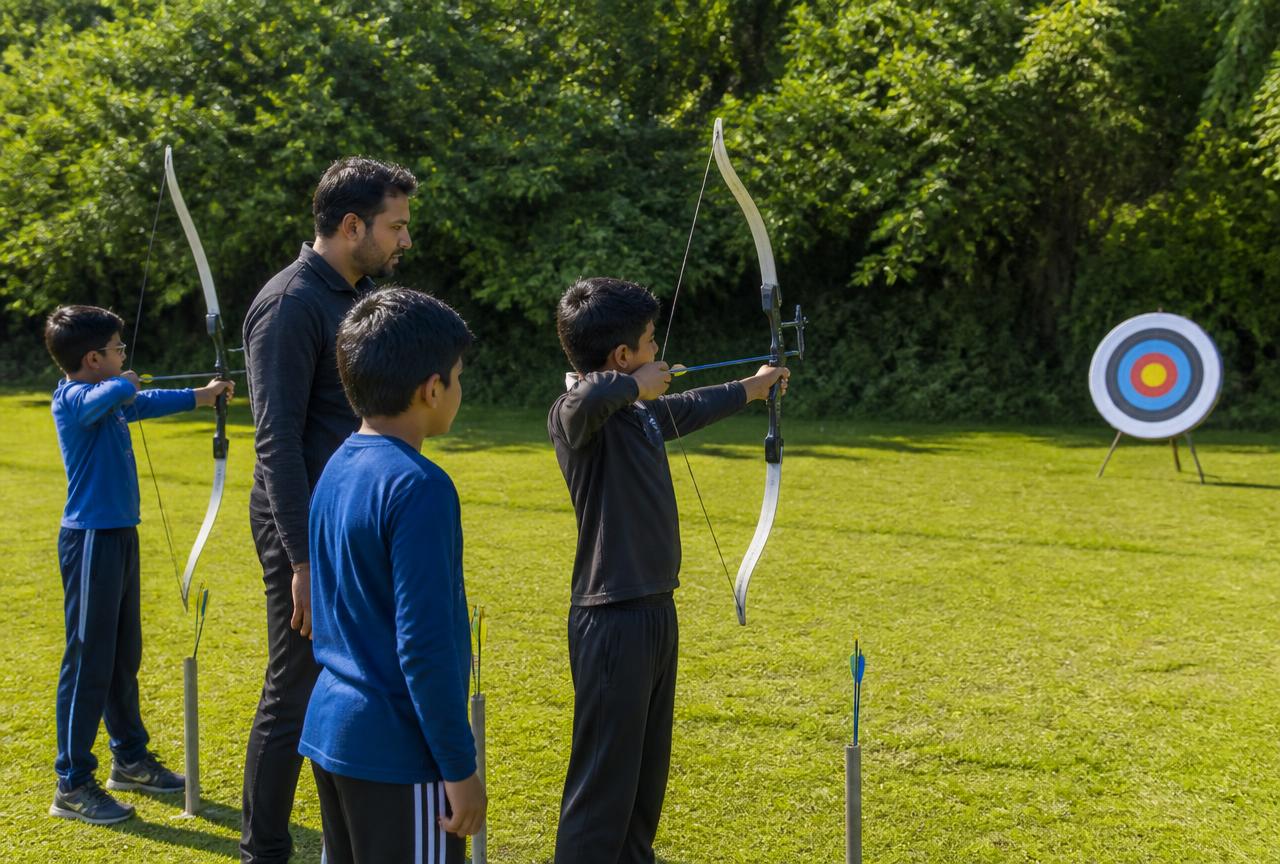 Boys learning archery on a grass field with a male coach